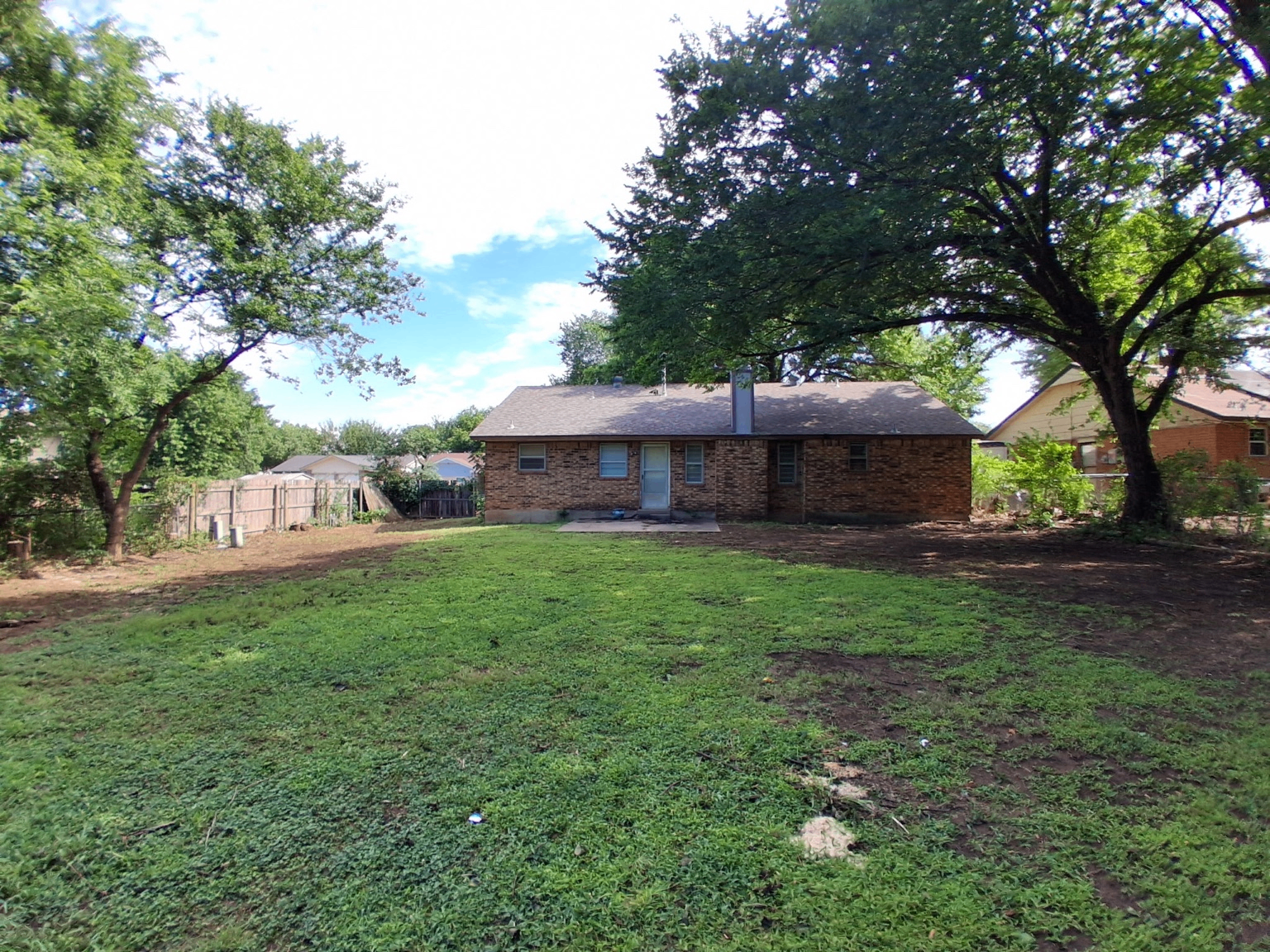 Backyard after large tree removal beside brick home with open sky by Wild Axe Arborists